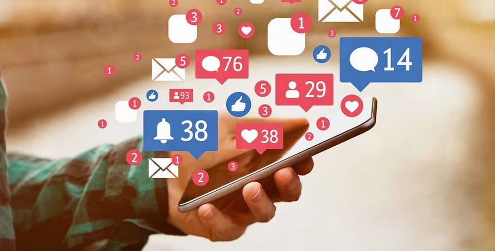 يد تمسك هاتفًا تتطاير منه إشعارات الإعجابات والتعليقات والمتابعين